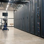 Fileiras de armários metálicos com servidores, dispositivos de rede e cabos em um data center moderno.