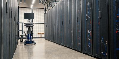Fileiras de armários metálicos com servidores, dispositivos de rede e cabos em um data center moderno.