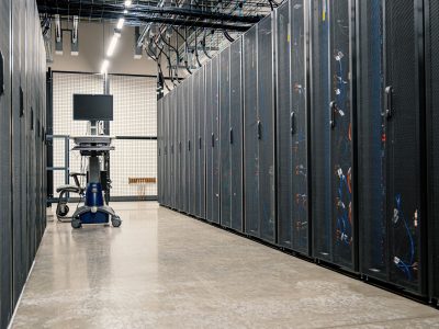 Fileiras de armários metálicos com servidores, dispositivos de rede e cabos em um data center moderno.