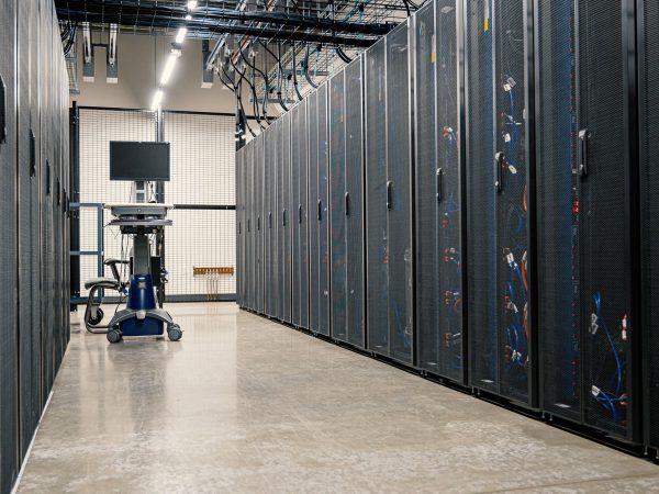 Fileiras de armários metálicos com servidores, dispositivos de rede e cabos em um data center moderno.