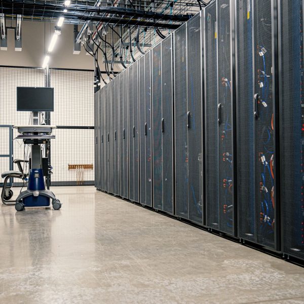 Fileiras de armários metálicos com servidores, dispositivos de rede e cabos em um data center moderno.