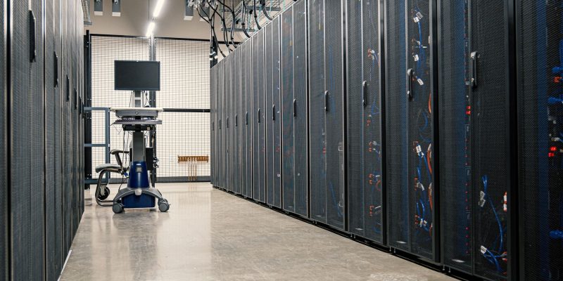 Fileiras de armários metálicos com servidores, dispositivos de rede e cabos em um data center moderno.