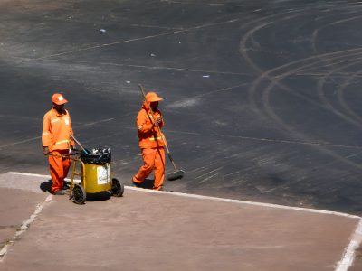 Dois trabalhadores da limpeza urbana usam uniformes laranja enquanto trabalham em Brasília.
