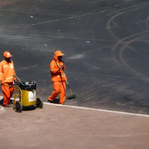 Dois trabalhadores da limpeza urbana usam uniformes laranja enquanto trabalham em Brasília.