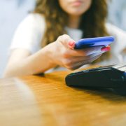 Mulher aproxima o smartphone de uma máquina de pagamento para realizar uma transação sem contato.