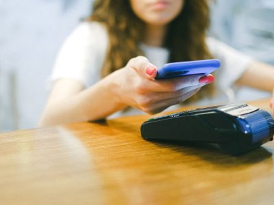 Mulher aproxima o smartphone de uma máquina de pagamento para realizar uma transação sem contato.