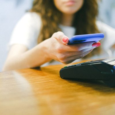 Mulher aproxima o smartphone de uma máquina de pagamento para realizar uma transação sem contato.