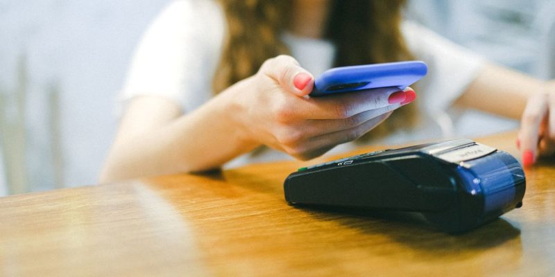 Mulher aproxima o smartphone de uma máquina de pagamento para realizar uma transação sem contato.