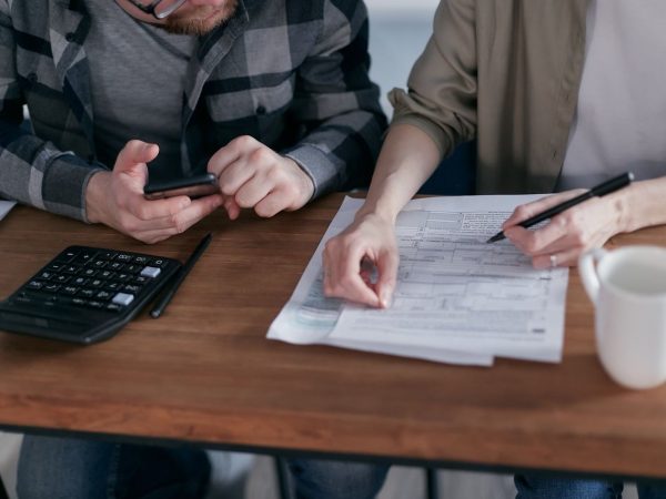 Casal analisa documentos e calcula as finanças em uma mesa dentro de casa.