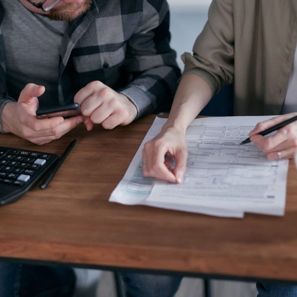 Casal analisa documentos e calcula as finanças em uma mesa dentro de casa.