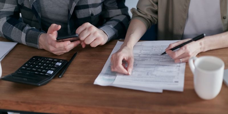 Casal analisa documentos e calcula as finanças em uma mesa dentro de casa.