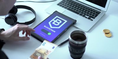 Tablet exibindo uma transação de moeda digital em blockchain ao lado de um laptop e cédulas de euro.